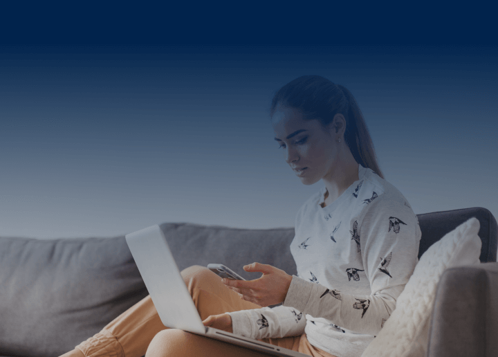 A woman holds a smartphone while using a laptop at the same time, symbolizing how easy it is to set up UsenetServer’s VPN on any device.